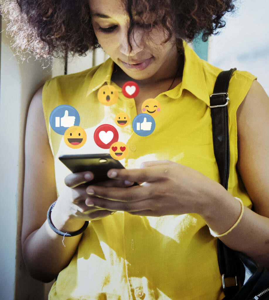 Woman smiling at her phone as like, heart and emoji icons float above it