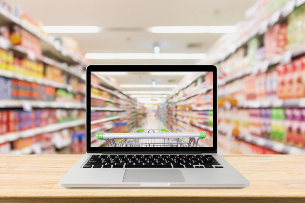 Laptop with a shopping cart on a desk in a supermarket aisle, representing online shopping