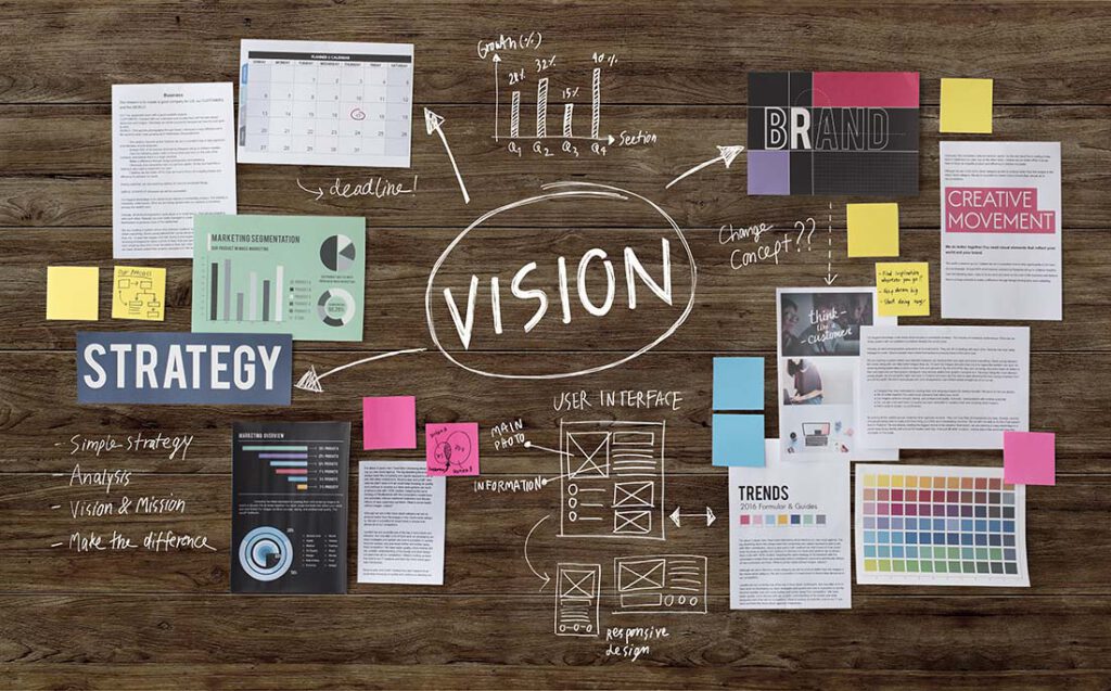 Wooden table covered with notes and sketches around the words Vision and Strategy