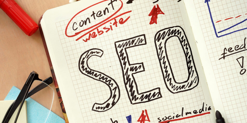 Notebook page with SEO written in large hand-drawn letters beside glasses and a pen