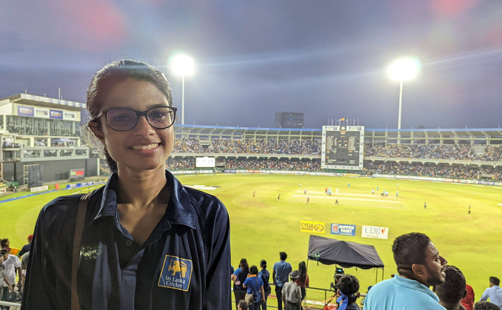 Shana smiling in front of a floodlit cricket stadium