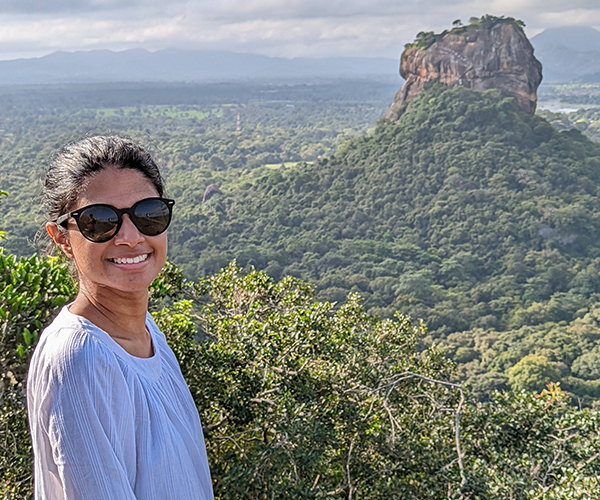 Shana smiling in sunglasses with a rocky forested hill behind her