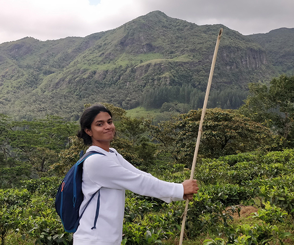 Shana smiling on a green hillside, holding a long wooden walking stick