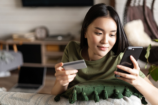 Woman lying on a couch holding a credit card and phone to shop online