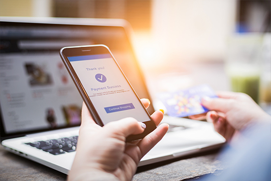 Hands holding a phone with a payment confirmation in front of a laptop