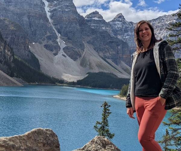 Jocelyn smiling in front of a turquoise mountain lake in the Rockies