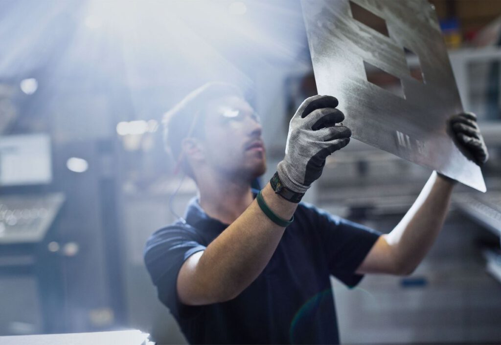 Worker in gloves holding up a custom-cut sheet of metal at GC Custom Metal Fabrication