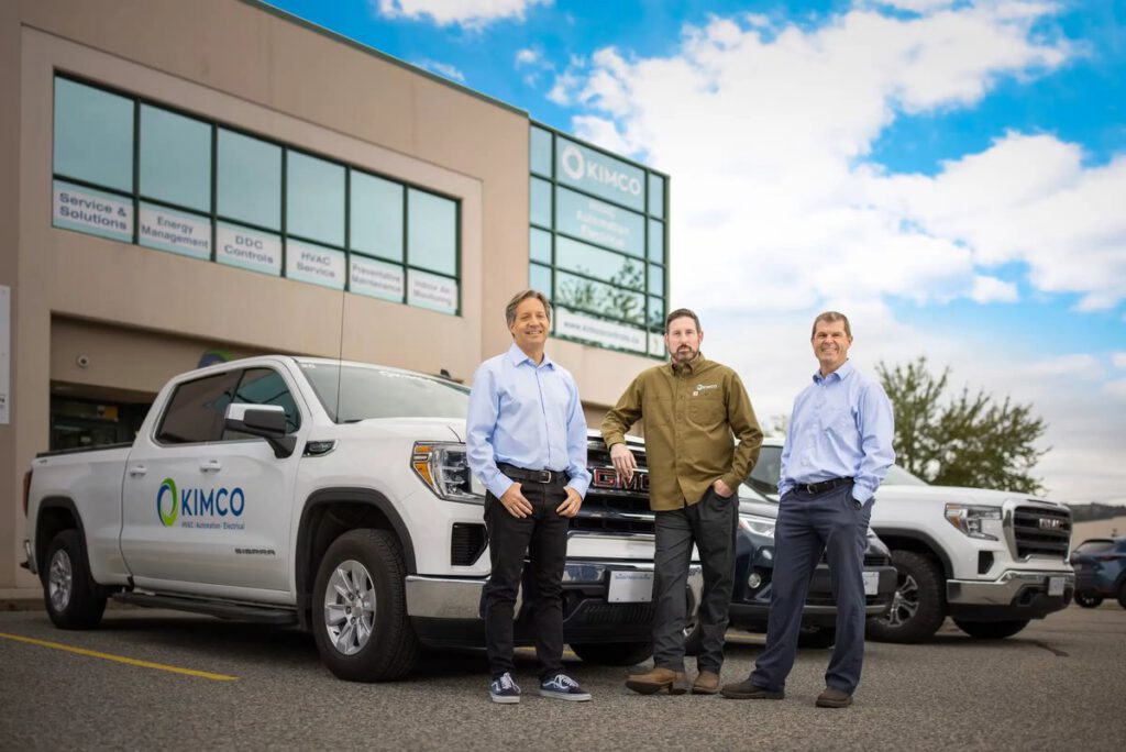 Three Kimco team members stand in front of Kimco service trucks outside their office