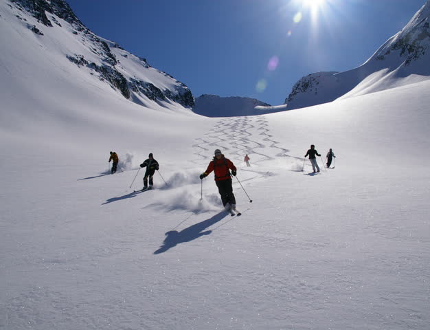 Skiers carving through deep powder in a sunlit alpine bowl, Northern Escape Heli-Skiing