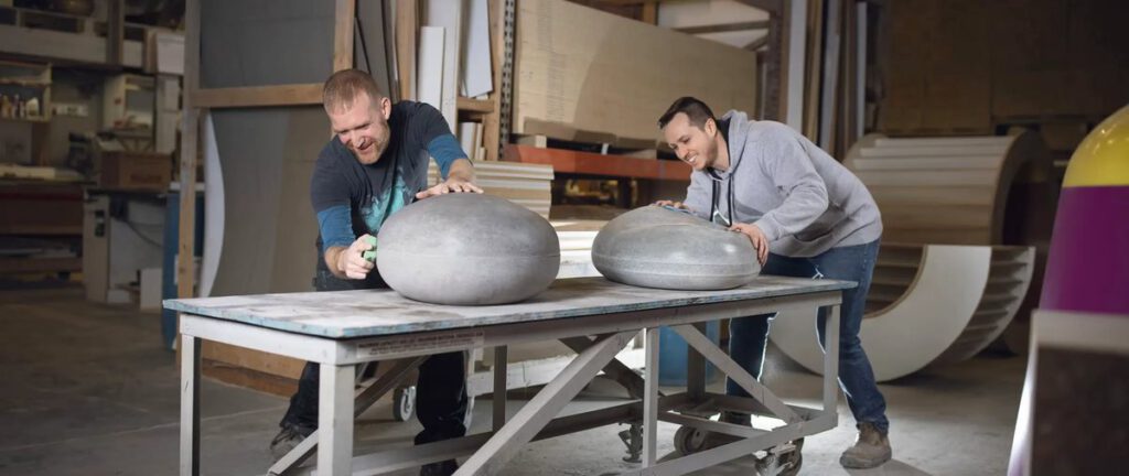 Two workers shape large metal forms on a workbench at Versatile Concrete